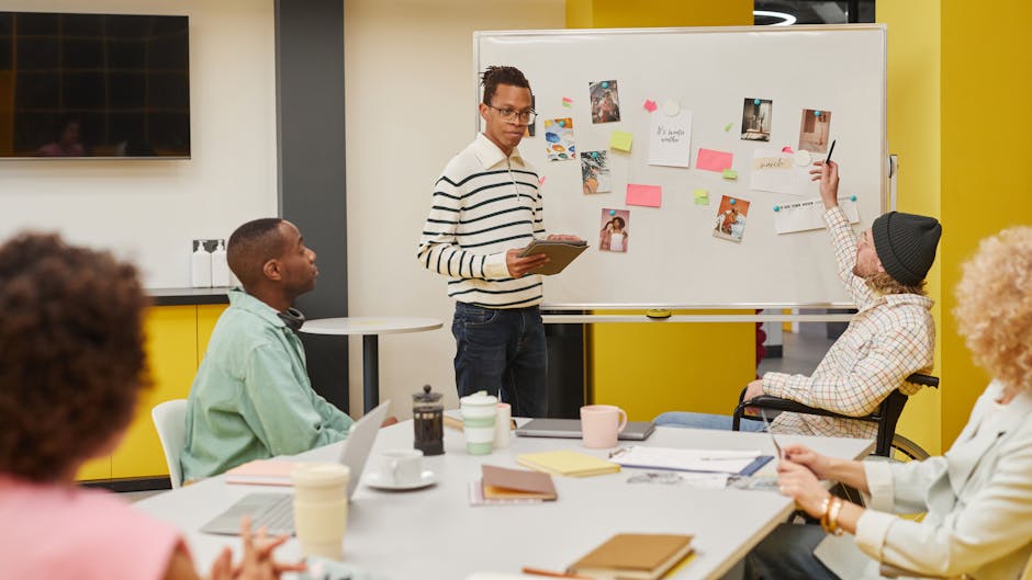 A diverse team engaged in a collaborative meeting around a whiteboard in a modern office setting.