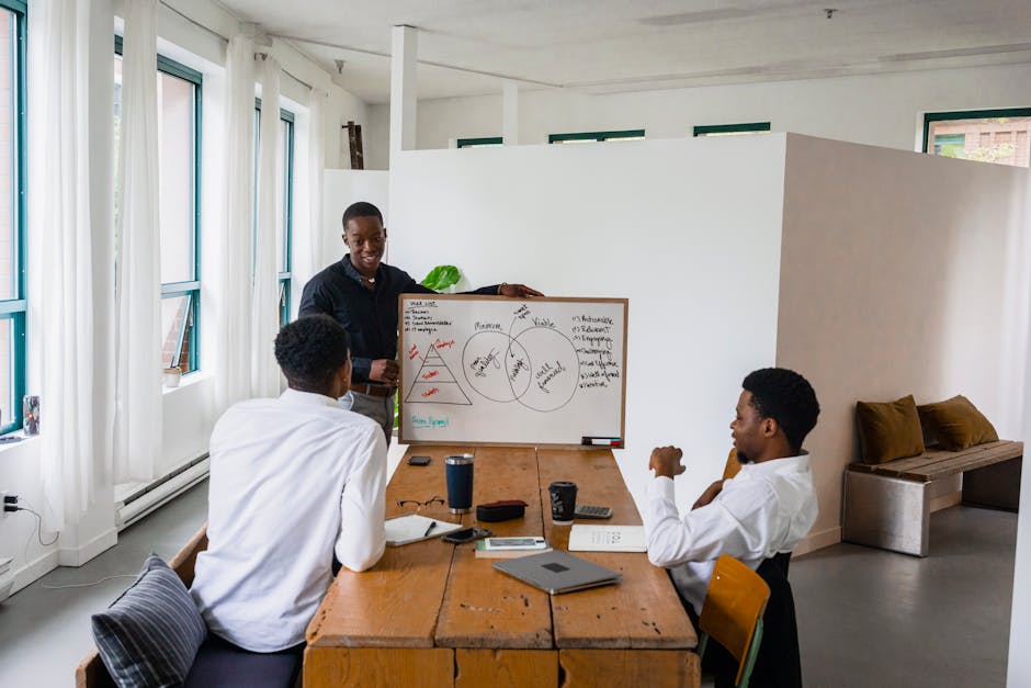 Three men engage in a business meeting with a whiteboard in a modern office.